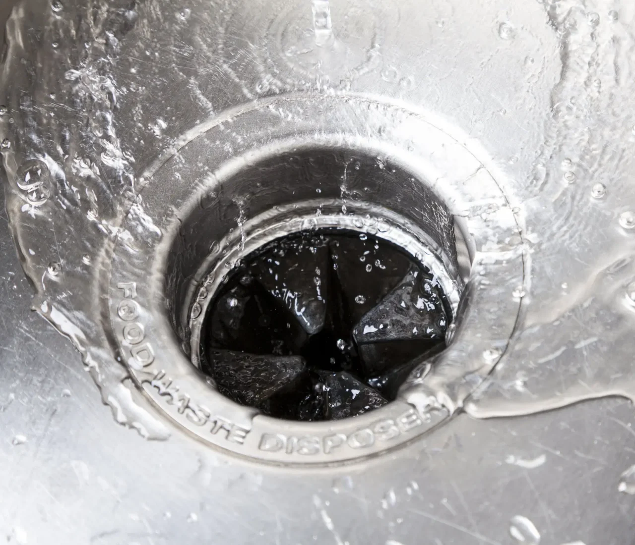 Black garbage disposal unit and drain connections beneath a kitchen sink.