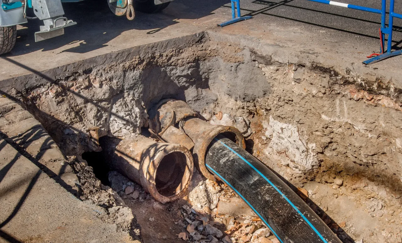 Black pipe with a blue stripe passing through an exposed older pipe.