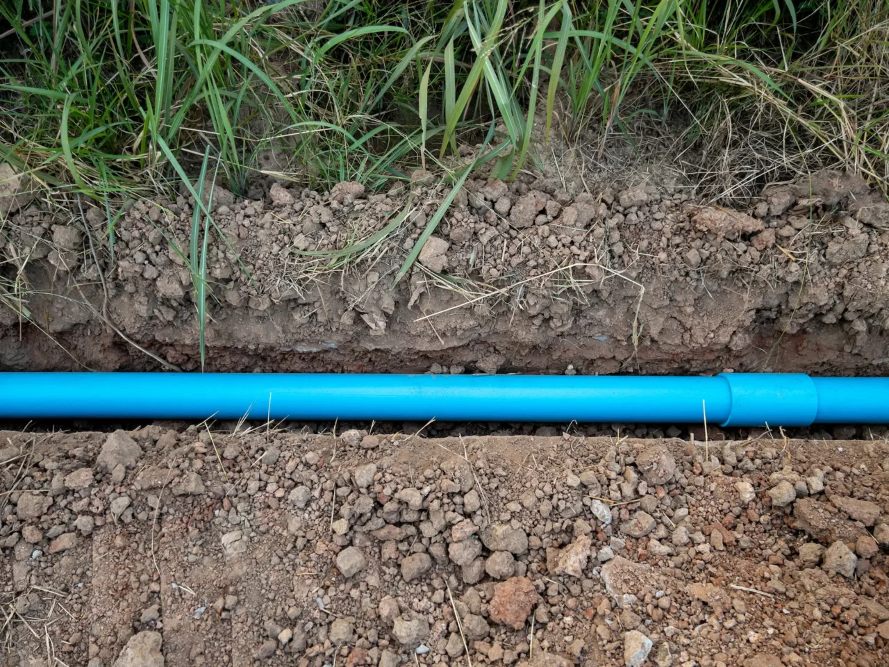 Blue water pipe laid in earthy trench beside grass.